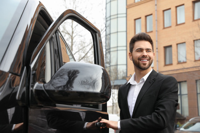 Photo of Handsome young man opening door of modern car outdoors