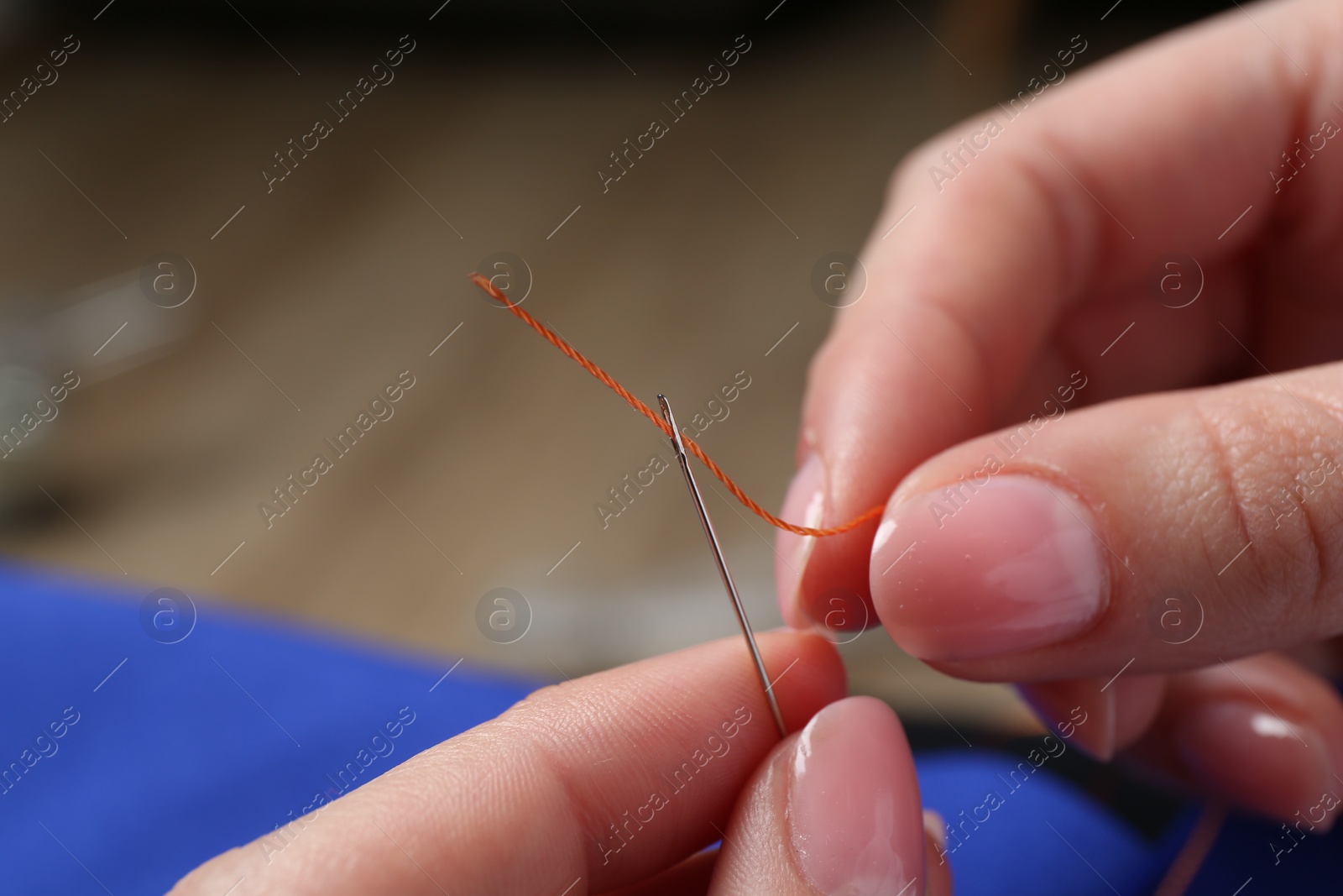 Photo of Woman inserting thread through eye of needle on blurred background, closeup