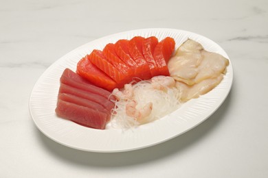 Photo of Tasty salmon slices, shrimp, funchosa and tuna on white marble table. Delicious sashimi dish