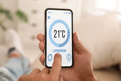 Image of Man using smartphone to control heating system in house, closeup