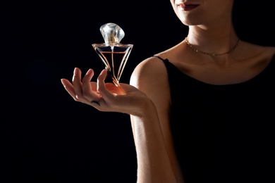 Photo of Young woman with perfume bottle on black background, closeup