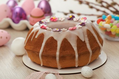 Delicious Easter cake decorated with sprinkles near painted eggs on white wooden table, closeup