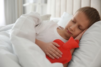 Photo of Ill boy with hot water bottle suffering from cold in bed at home