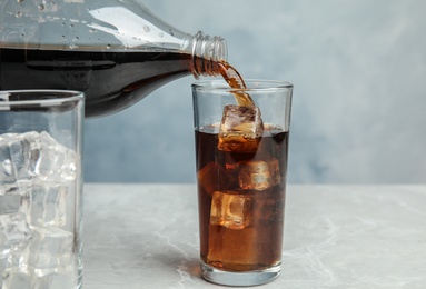 Pouring refreshing soda drink into glass on table against blue background