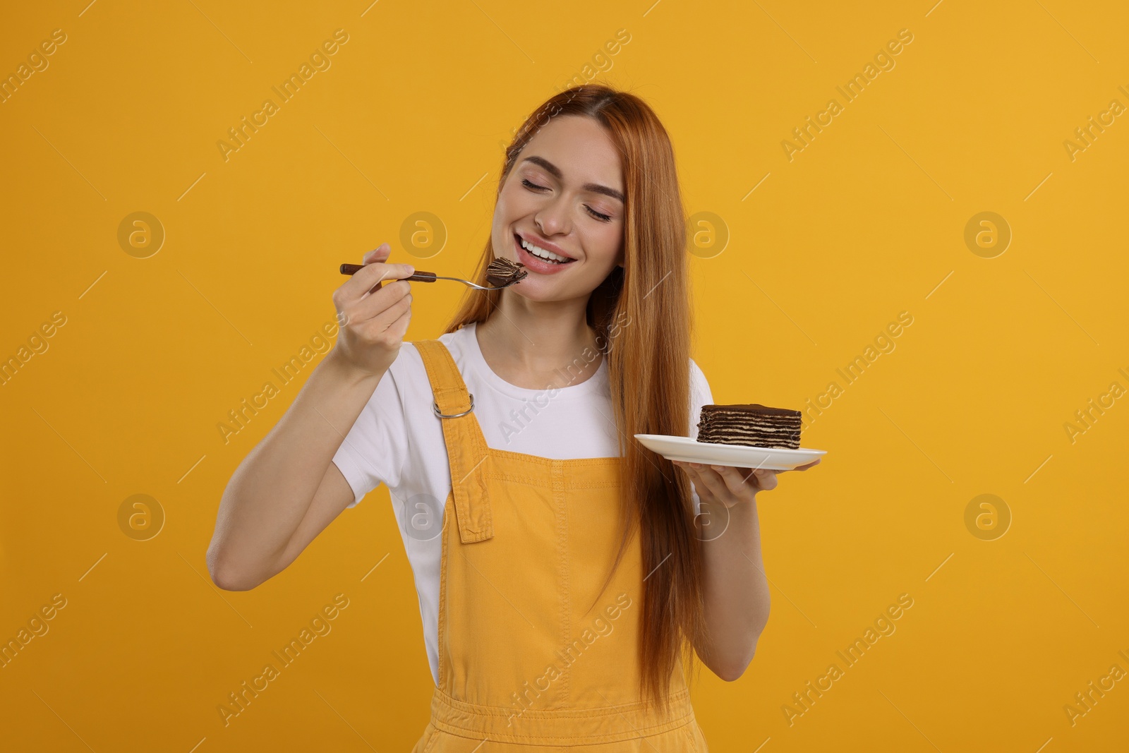 Photo of Young woman eating piece of tasty cake on orange background