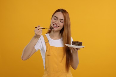 Young woman eating piece of tasty cake on orange background