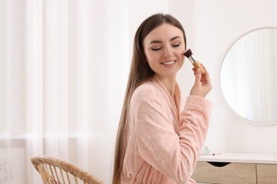 Photo of Beautiful young woman applying makeup with brush indoors. Space for text