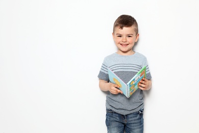 Cute little boy reading book on white background, space for text