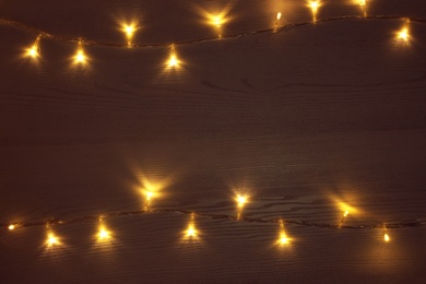Photo of Frame of beautiful glowing Christmas lights on wooden table, top view. Space for text