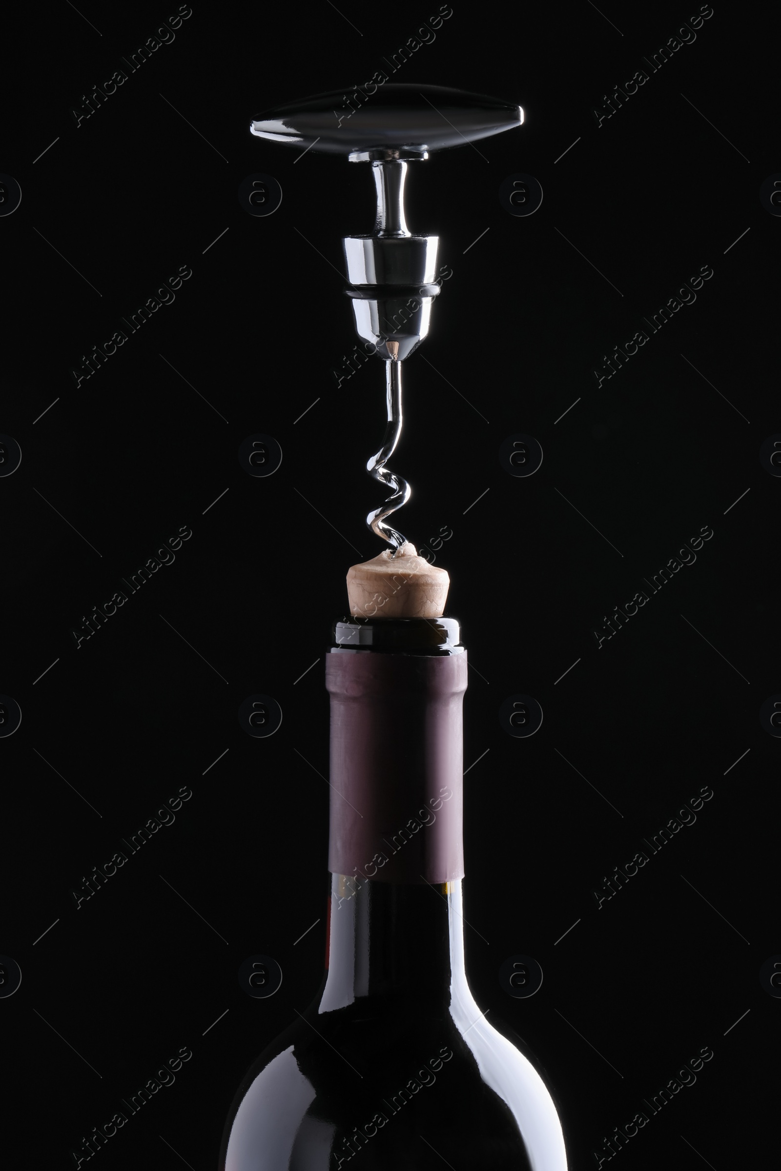 Photo of Opening wine bottle with corkscrew on dark background, closeup