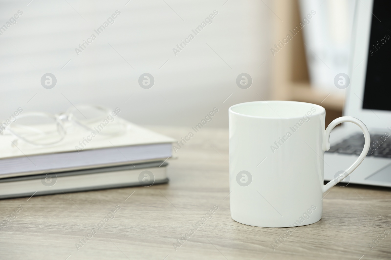 Photo of White ceramic mug, notebooks and laptop on wooden table indoors. Space for text