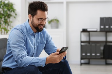 Photo of Handsome young man using smartphone in office, space for text