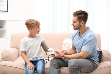 Young man checking little boy's pulse indoors