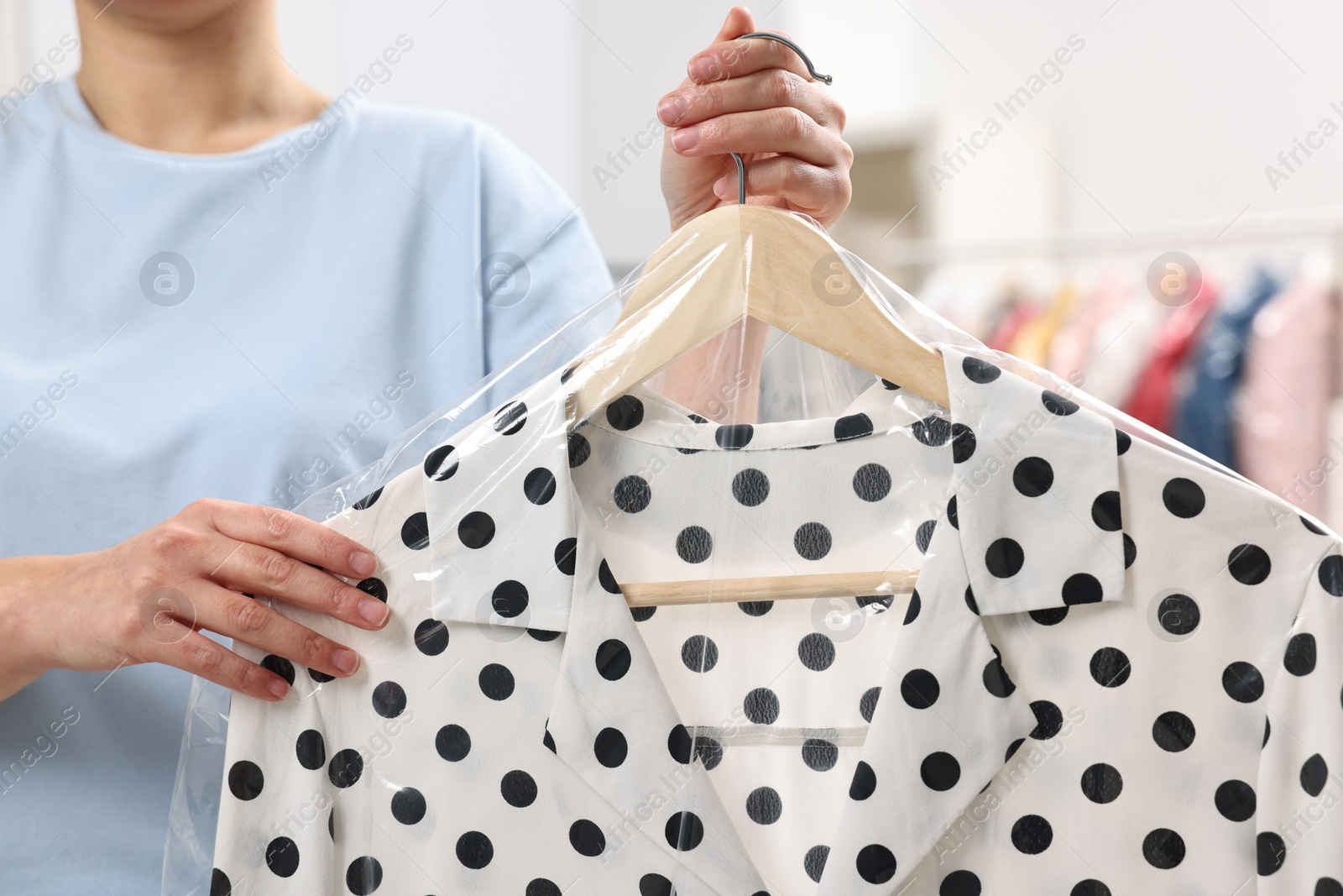 Photo of Dry-cleaning service. Woman holding shirt in plastic bag indoors, closeup