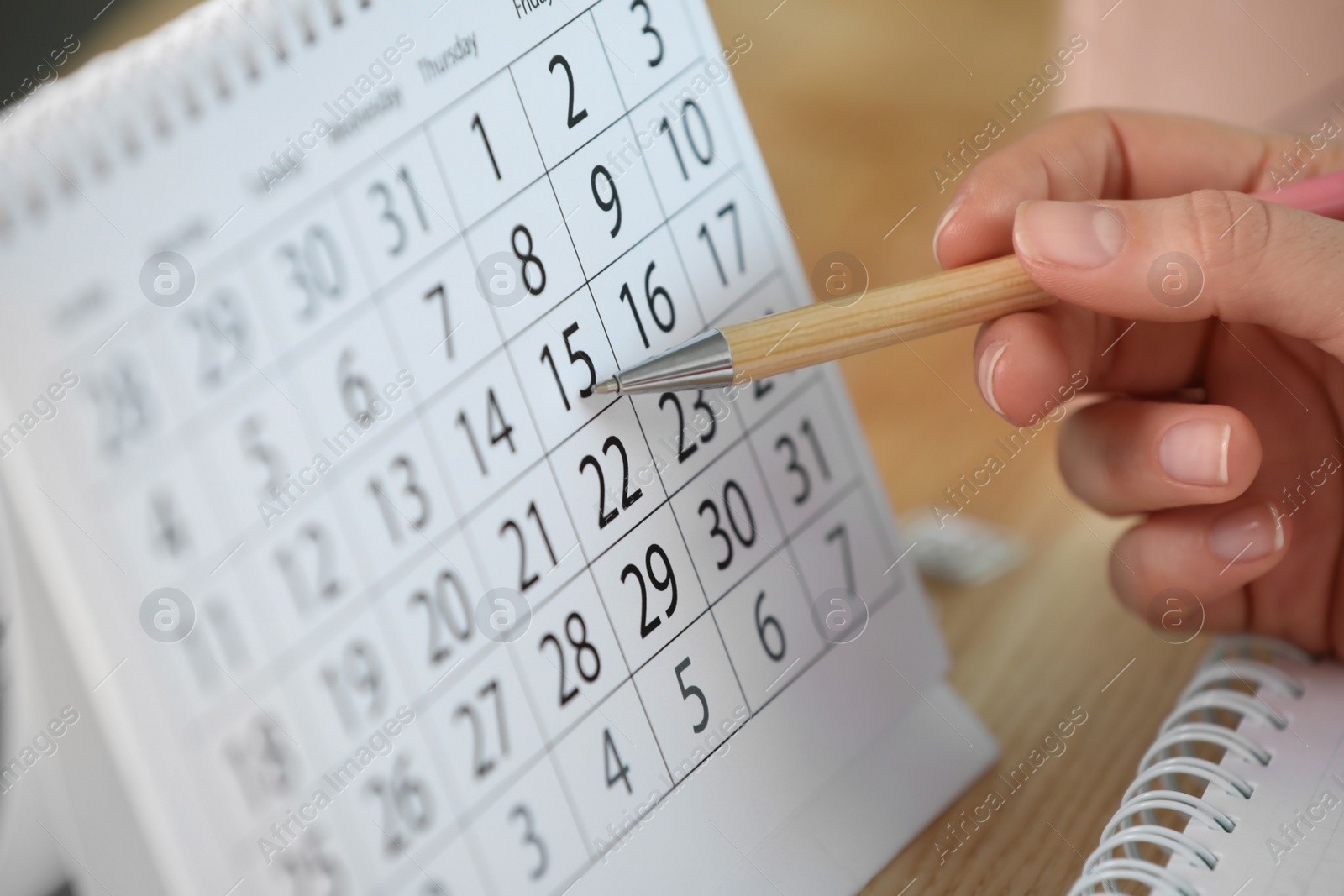 Photo of Woman making schedule using calendar at wooden table, closeup