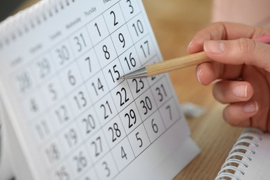 Woman making schedule using calendar at wooden table, closeup
