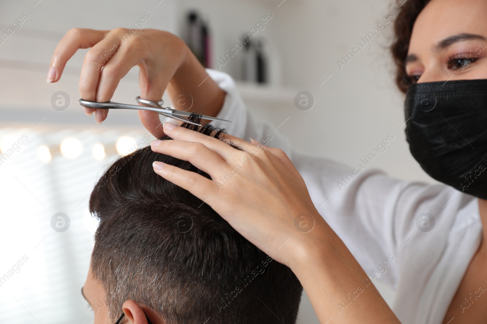 Photo of Professional stylist working with client in salon, closeup. Hairdressing services during Coronavirus quarantine