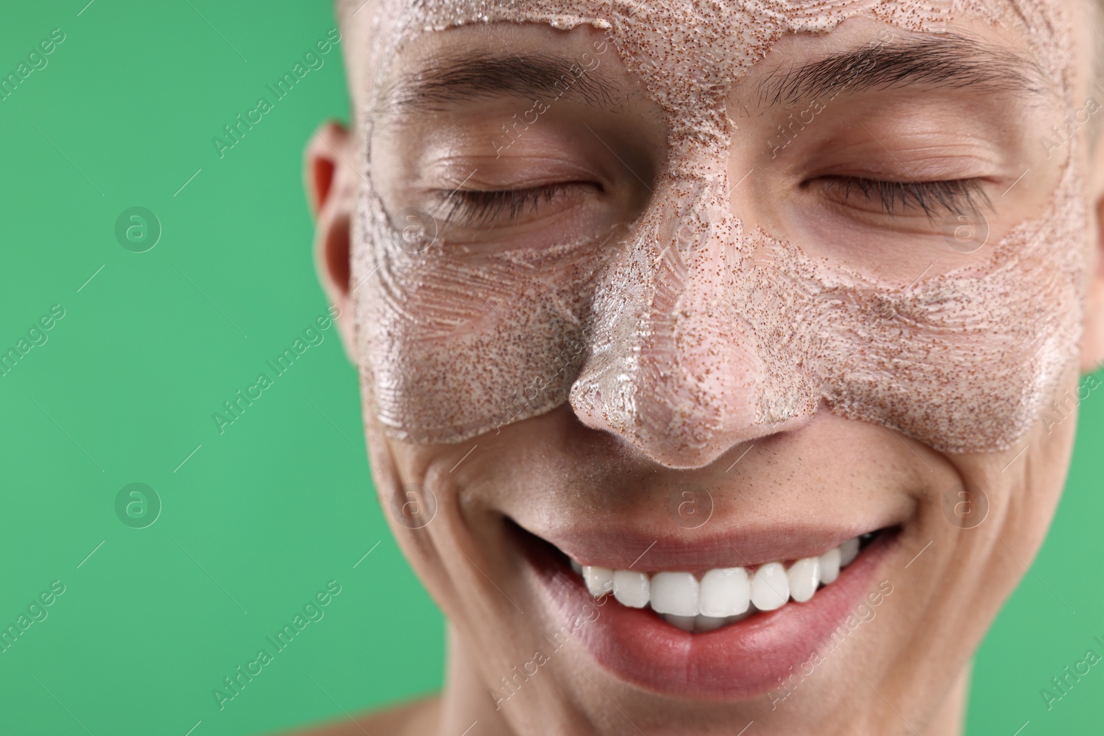 Photo of Handsome man with facial mask on his face against green background, closeup. Space for text