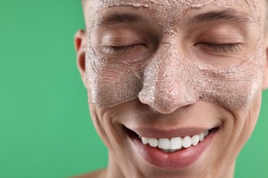 Handsome man with facial mask on his face against green background, closeup. Space for text