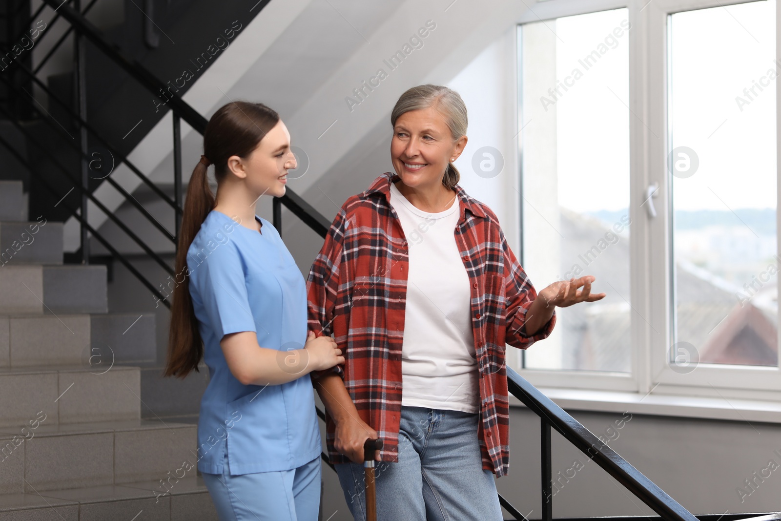 Photo of Young healthcare worker assisting senior woman on stairs indoors