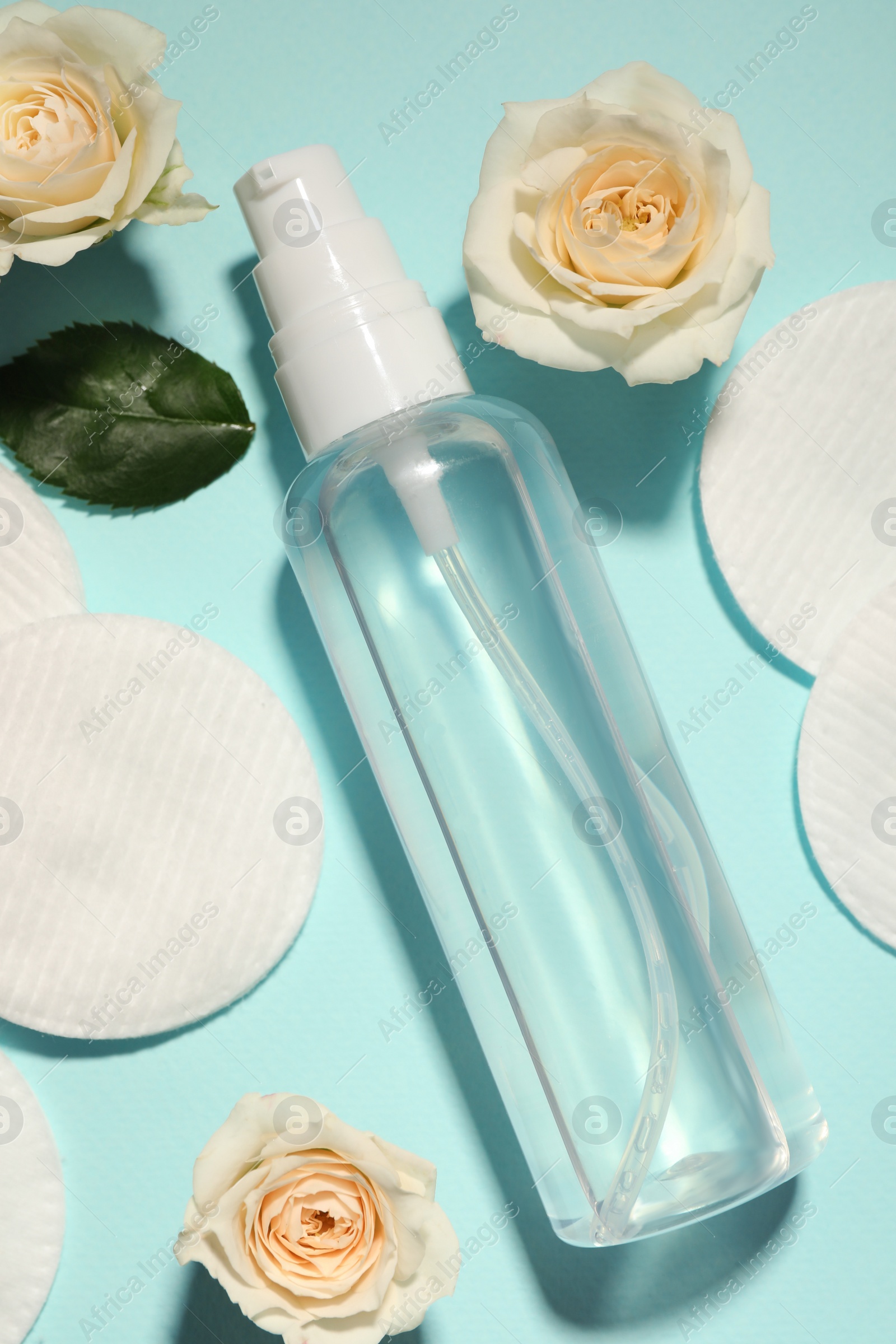Photo of Bottle of micellar cleansing water, cotton pads and flowers on turquoise background, flat lay