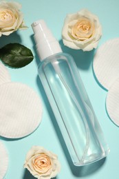 Photo of Bottle of micellar cleansing water, cotton pads and flowers on turquoise background, flat lay