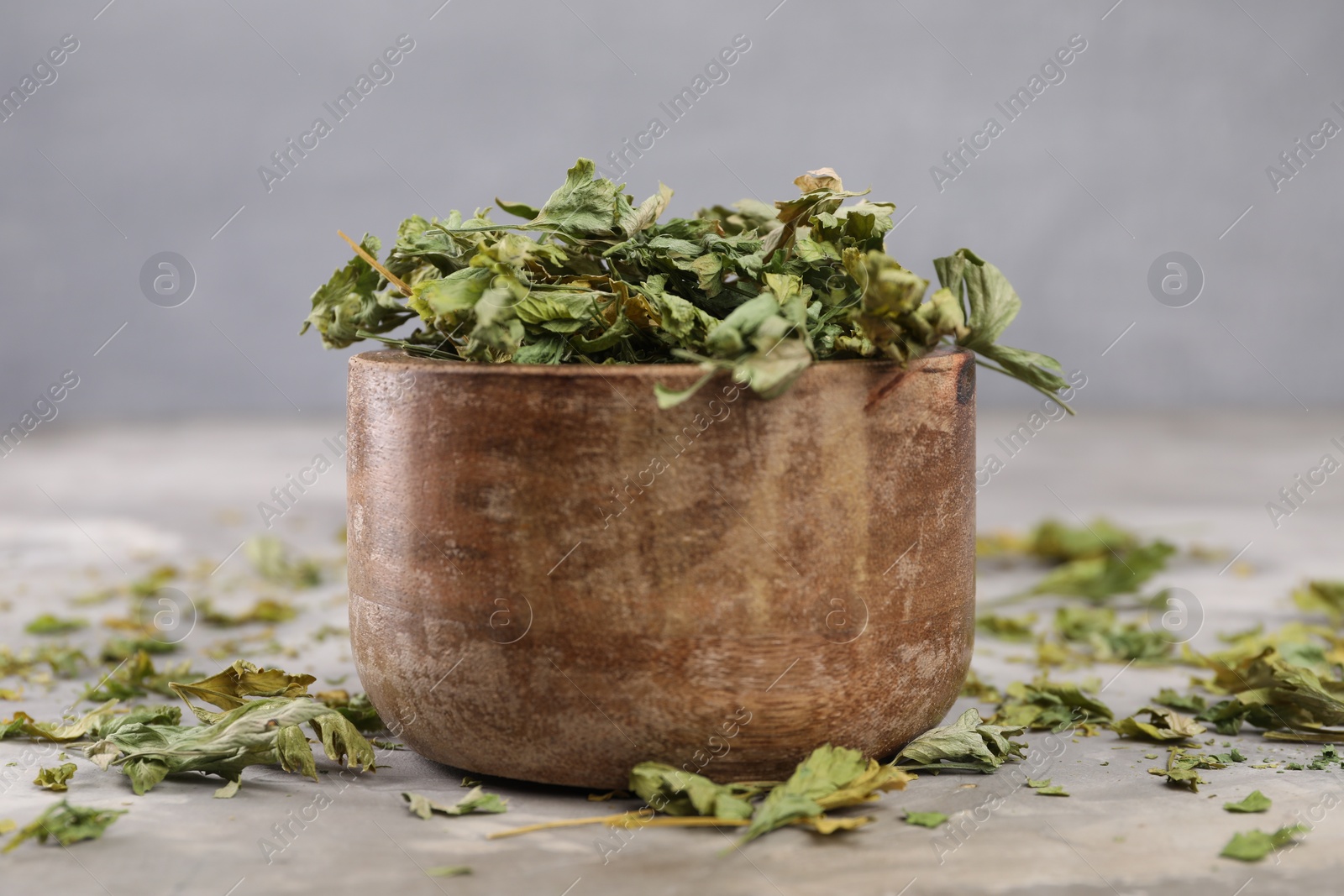 Photo of Bowl with dry parsley on light grey textured table, closeup