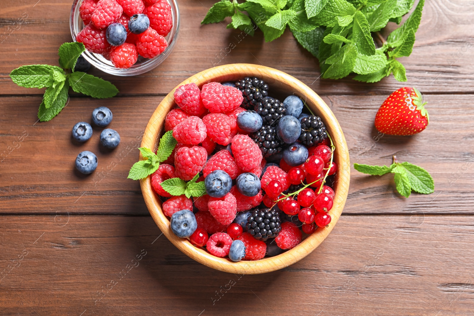 Photo of Bowl with raspberries and different berries on wooden table, top view