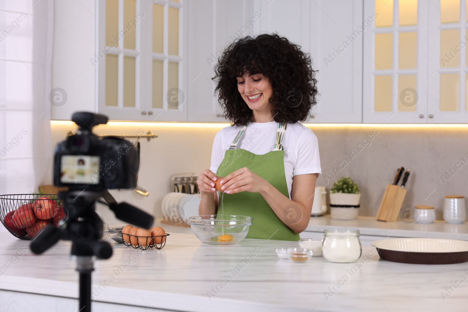 Photo of Smiling food blogger cooking while recording video in kitchen