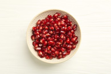 Photo of Ripe juicy pomegranate grains in bowl on white wooden table, top view