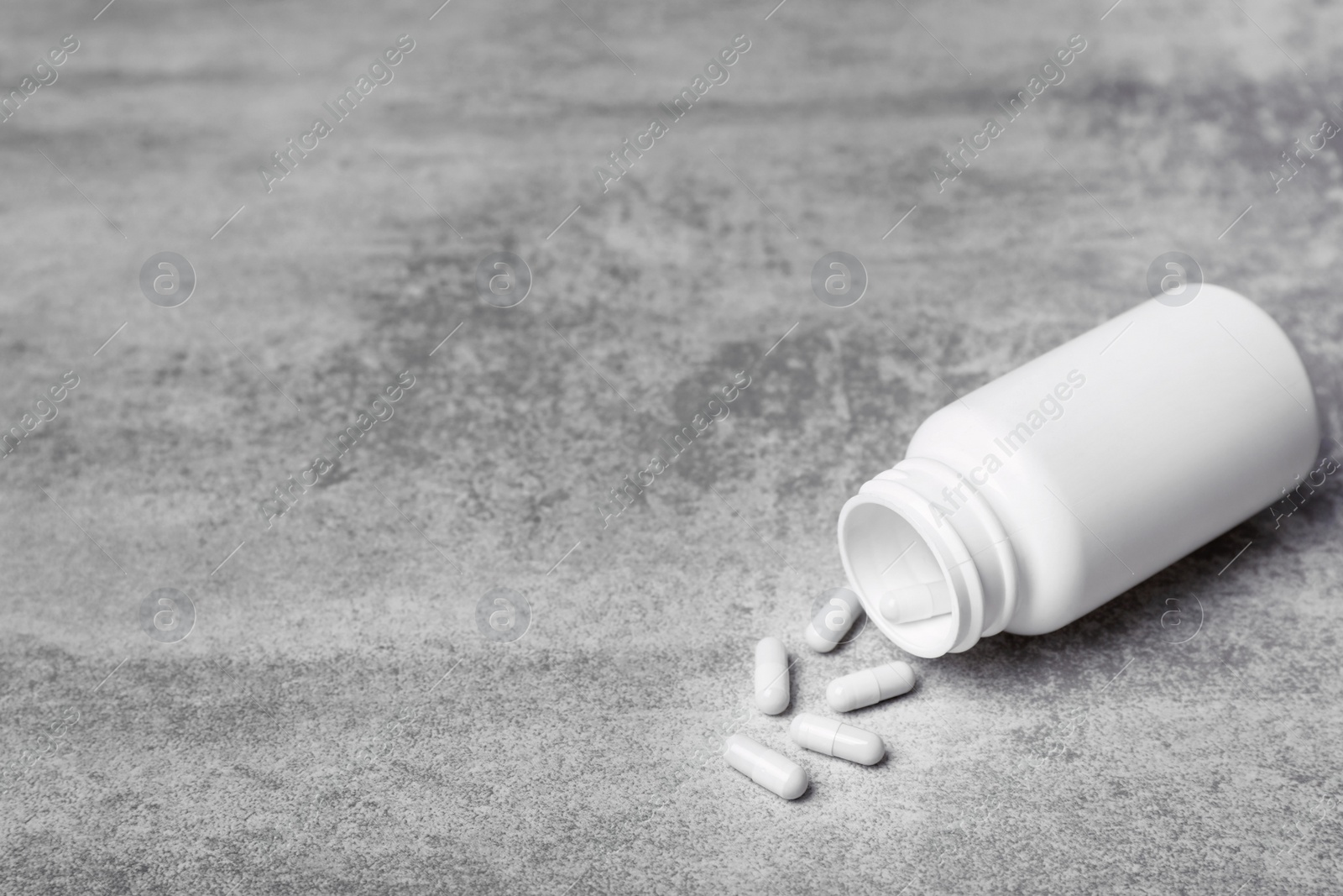 Photo of Container with white pills on grey background