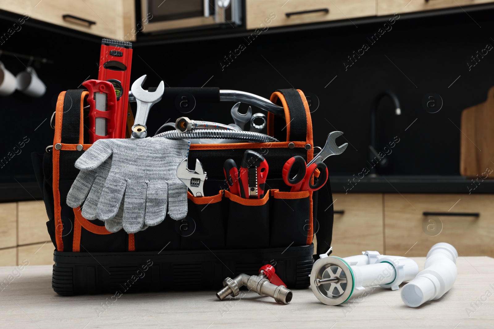 Photo of Plumber's tool bag and pipes on table in kitchen