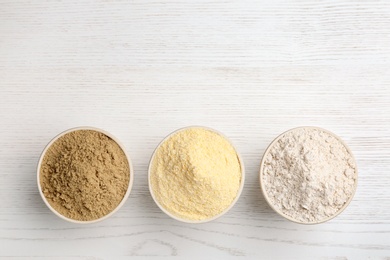 Bowls with different types of flour on white wooden background, top view. Space for text