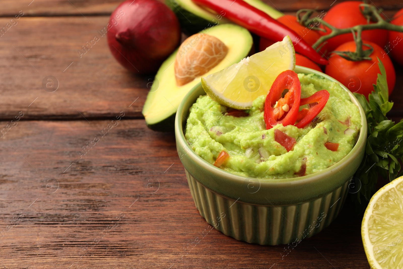 Photo of Bowl of delicious guacamole and ingredients on wooden table, closeup. Space for text