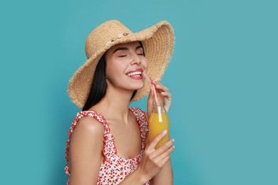 Photo of Beautiful young woman with straw hat and bottle of refreshing drink on light blue background
