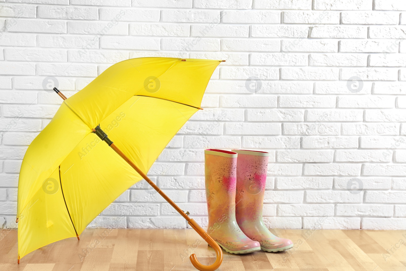 Photo of Beautiful yellow umbrella and rubber boots near white brick wall