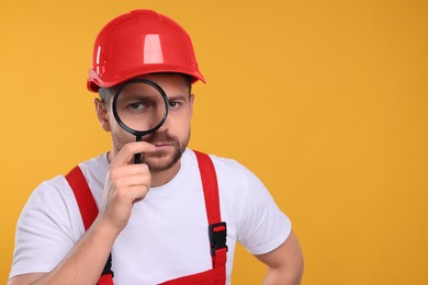 Photo of Builder looking through magnifier glass on yellow background, space for text