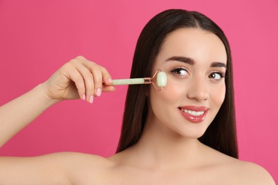 Photo of Woman using natural jade face roller on pink background