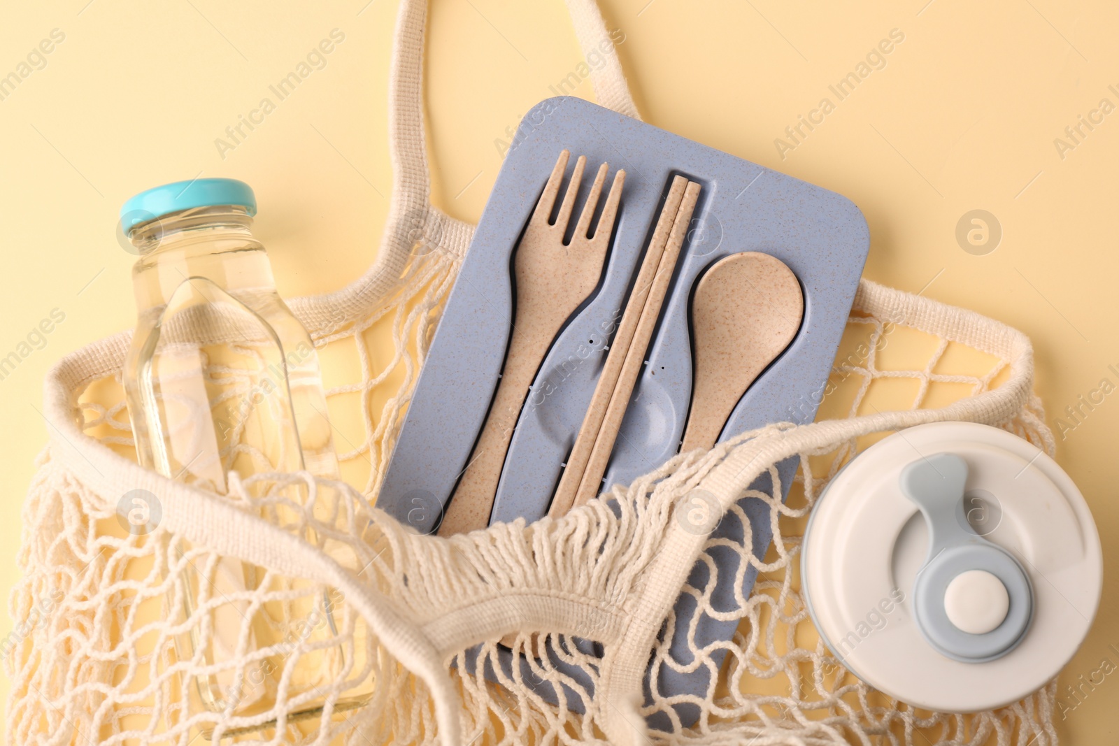 Photo of Fishnet bag with different items on beige background, top view. Conscious consumption