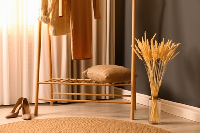Photo of Dry plants near clothes rack indoors. Interior design