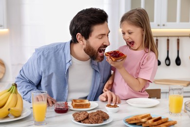 Photo of Father and his cute little daughter having fun during breakfast at table in kitchen
