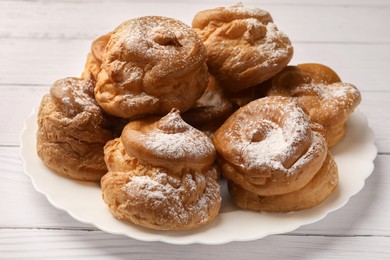 Photo of Delicious profiteroles with powdered sugar on white wooden table