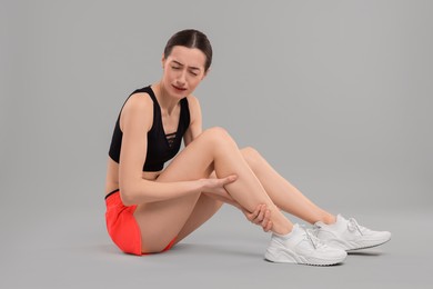 Photo of Young woman suffering from leg pain on grey background