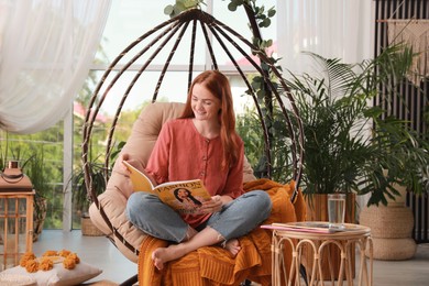 Happy young woman reading magazine in egg chair at indoor terrace