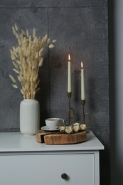 Cup of coffee, vase and other decor on white table near grey wall indoors. Interior design