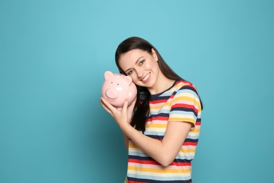 Young woman with piggy bank on color background