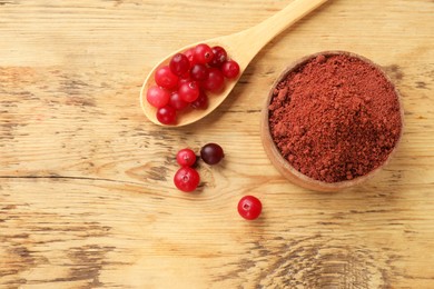 Photo of Cranberry powder in bowl and spoon with fresh berries on wooden table, top view. Space for text