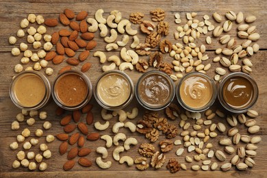 Nut butters in bowls and ingredients on wooden table, flat lay