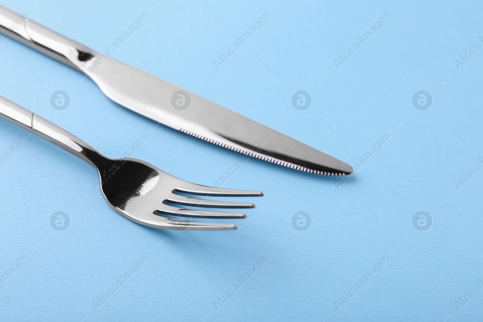Photo of Stylish cutlery. Silver knife and fork on light blue background, closeup