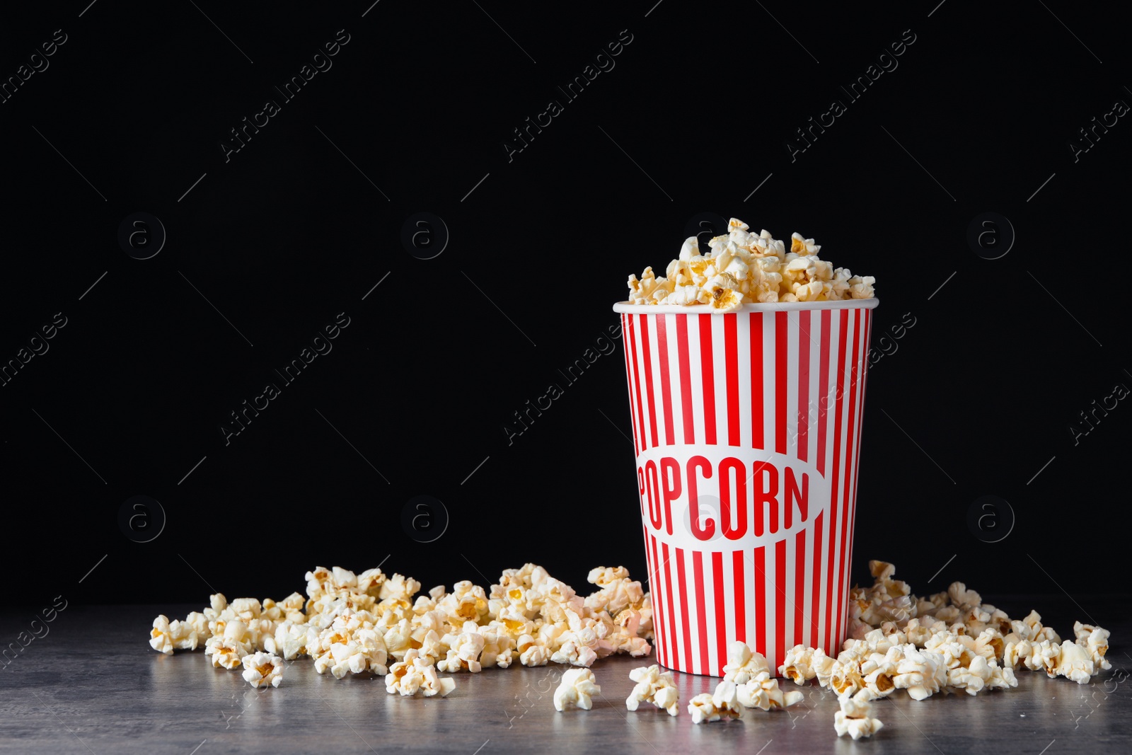 Photo of Bucket of fresh popcorn on grey stone table against black background, space for text. Cinema snack